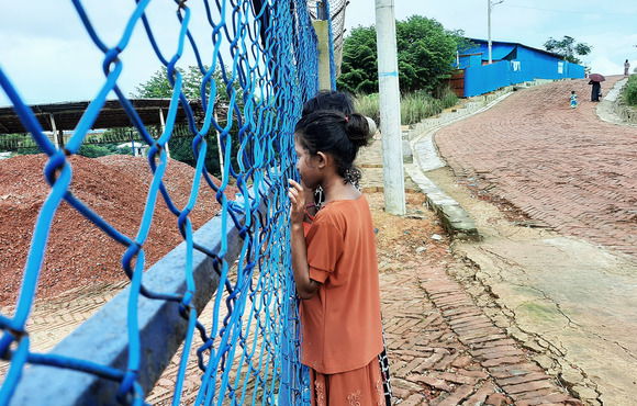 Rohingya girls peer through a newly constructed fence in the camps. Some say that the government-built fencing around parts of the refugee camps may have made it harder to escape a March 2021 fire that displaced tens of thousands of people.