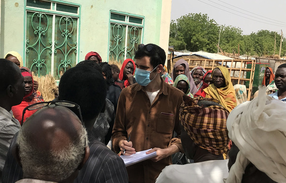 A reporter speaks to a group of people outside a small building.