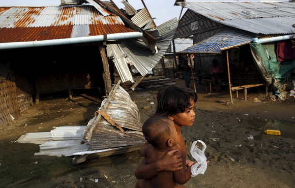 Rohingya girls pass in front of a damaged shelter in a displacement camp outside Sittwe in Myanmar’s Rakhine State in August 2015.