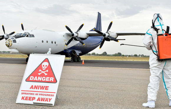 A person in a protective suit cleans an airport runway – in the background of the image a plane can be seen, and a warning sign.