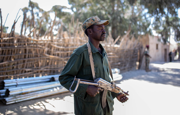 A man stands in a street, holding a gun.