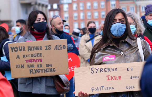 Demonstrators wearing masks hold signs at a protest. 