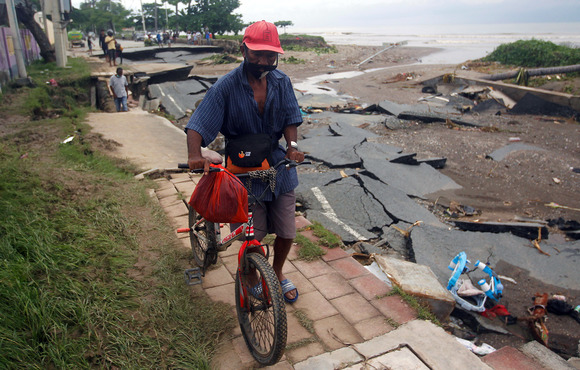 A man walks his bike along a road that has been damaged by flooding and heavy rains. 
