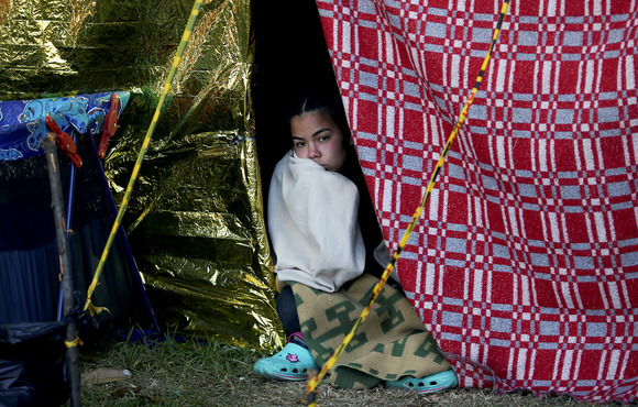 A Venezuelan migrant woman looks out the opening of a makeshift shelter at the camera.