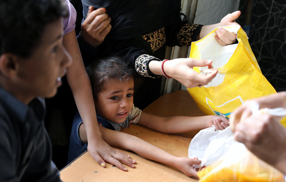 A girl looks on as worker gives a food ration to a boy at charity kitchen in Sana'a, Yemen 20 July, 2020