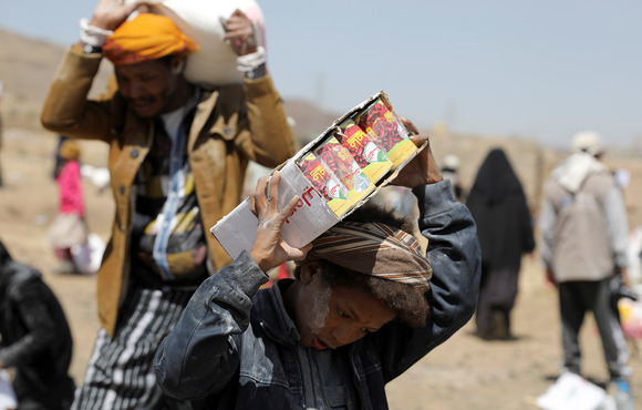 A youth and a man carry food aid on their shoulders in the sun.