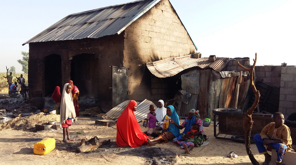 Women and children sit outside a burnt house after a suspected Boko Haram attack in Bulabulin village, in northeast Nigeria on 1 November 2018.