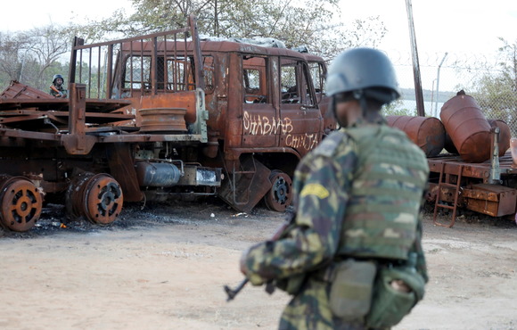 A Rwandan soldier walks past a burnt-out truck at the recaptured port of Mocimboa da Praia in Cabo Delgado. The graffiti reads "Shabab slaughters" in Swahili. 22 September 2021.