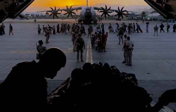 Silhouette of a soldier with a military plane in the background and Afghan evacuees on the tarmac.