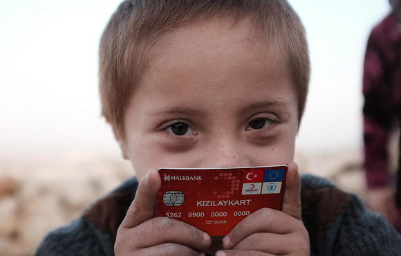 A refugee child holds a prototype bank card issued by the EU-funded Emergency Social Safety Net programme to provide money transfers to refugees in Turkey.